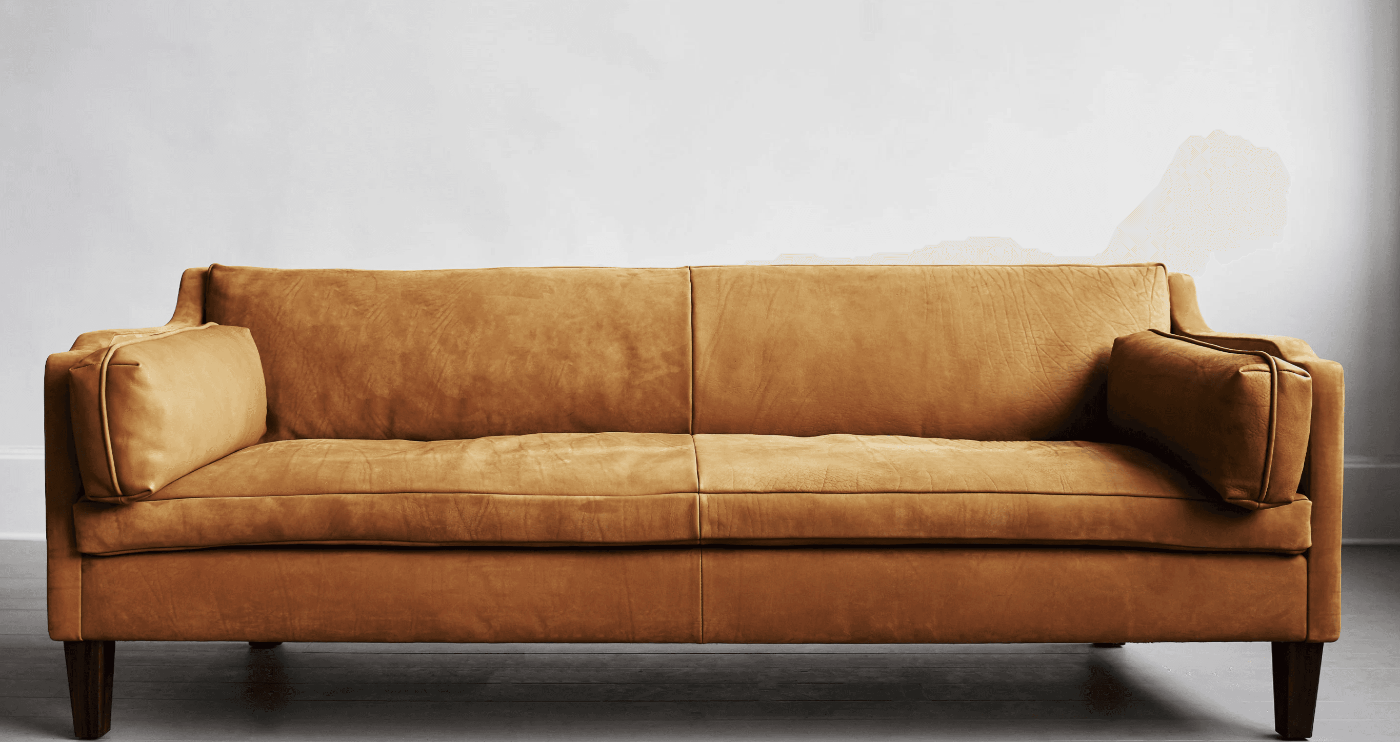 A mid-century modern inspired three-seater sofa with a low profile and square arms. The upholstery appears to be a distressed or aged leather in a warm tan or cognac color. It features two seat cushions and two back cushions, with a single lumbar pillow visible on the right armrest. The sofa is supported by four dark, tapered wooden legs. — 3D model