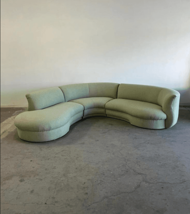 A large, curved sectional sofa with a light green upholstered finish. The sofa features a rounded chaise lounge extension on the left and multiple curved seating segments that form a semi-circular shape. The backrests are slightly curved, and the overall design is plush and inviting. — 3D model