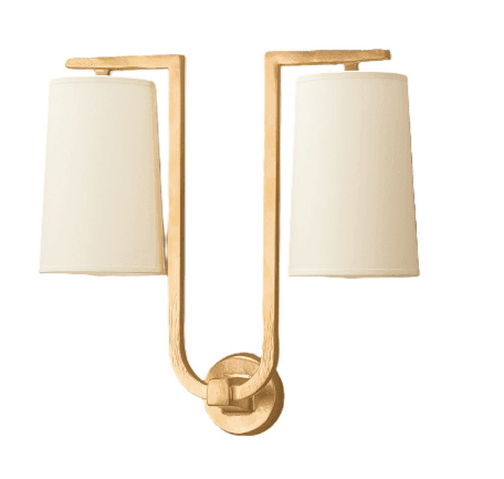 A two-light wall sconce featuring a textured gold-finished metal frame and two cream-colored fabric shades. The frame extends upwards from a central wall-mounted base, forming two curved arms that support the individual shades. The shades are tapered cylinders, open at the top and bottom. The metal has an intentionally uneven, artisan-like texture. — 3D model