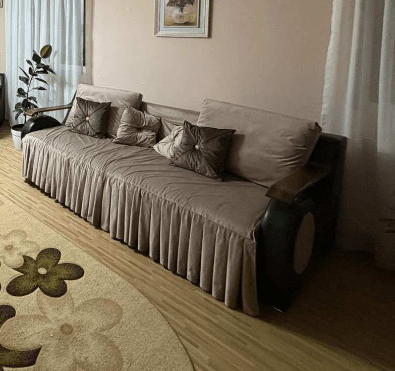 A sophisticated sofa featuring light beige fabric upholstery, a pleated skirt, and distinctive dark-toned curved armrests with wooden tops and metallic accents. — 3D model