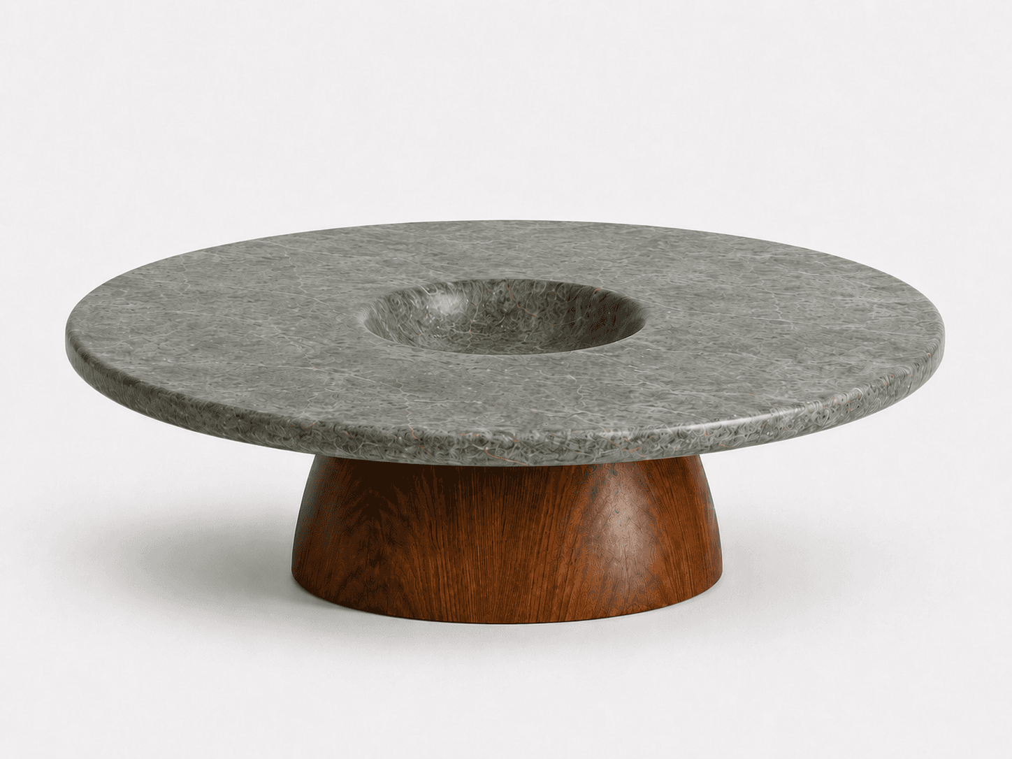 A modern, round coffee table featuring a distinctive dark gray, textured stone top with a central, smoothly carved depression. The top rests on a sturdy, flared dark wood pedestal base. The stone surface displays subtle veining or granular patterns, contributing to its organic aesthetic. — 3D model