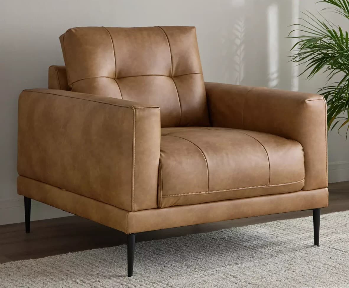 A contemporary armchair upholstered in tan leather, featuring a boxy silhouette, square track arms, a tufted back cushion, and supported by slender black tapered legs. — 3D model