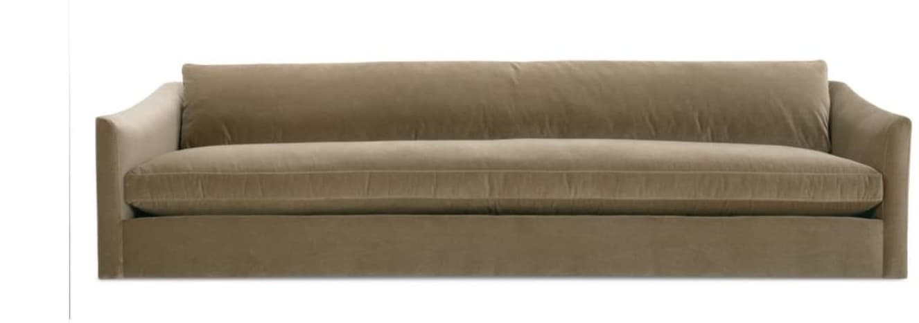 A three-seater sofa featuring plush, light brown (taupe) upholstery, possibly velvet or chenille. It has low, slightly curved track arms and a skirted base that conceals the legs. The back cushions are loose, while the single, long seat cushion appears fixed or semi-fixed, with a subtle welted seam defining its edge. — 3D model