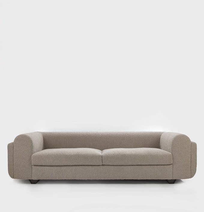 A two-seater sofa upholstered in a light beige/greige boucle fabric. The design features a low profile with rounded, continuous track arms and backrest, creating a soft, inviting aesthetic. It has two distinct seat cushions and appears to rest on discreet, low-set wooden block feet. — 3D model