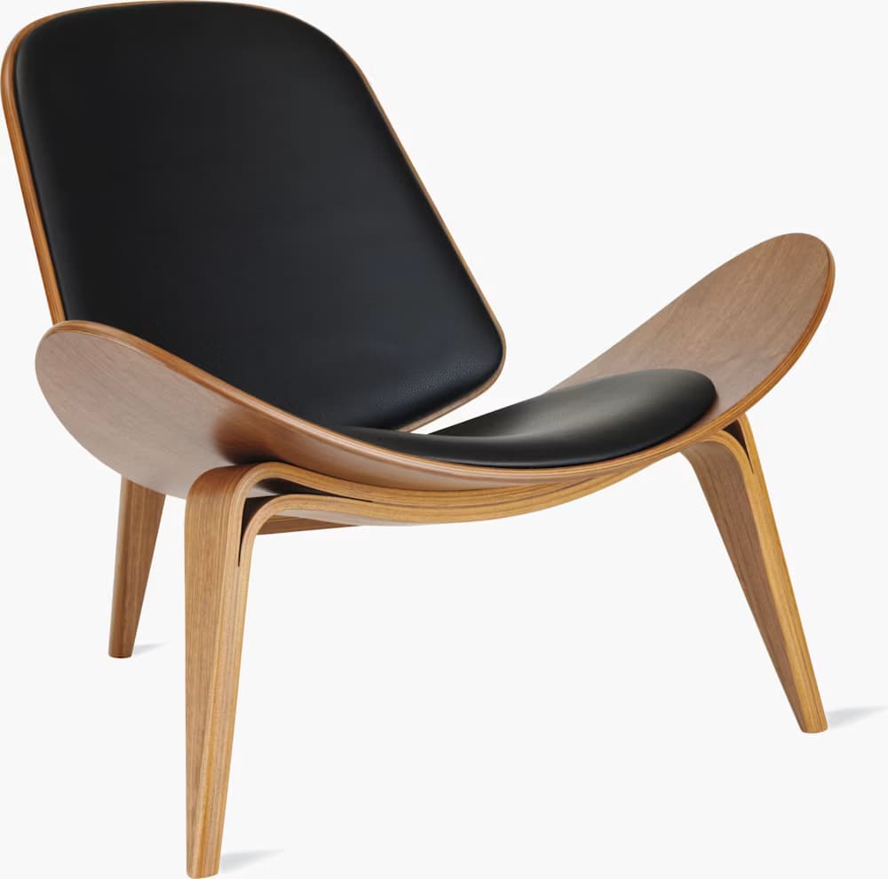 A high-quality image of a Hans J. Wegner CH07 Shell Chair, featuring a distinctive three-legged, curved plywood frame with black leather upholstered seat and back pads. The chair exhibits a light wood finish and a sleek, sculptural form against a white background. — 3D model