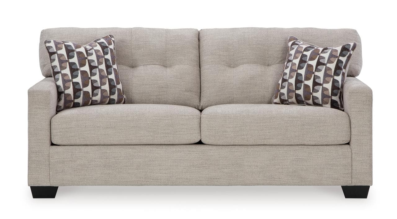 A contemporary upholstered sofa featuring a light beige or greige fabric, block arms, and tapered block feet. It has two large seat cushions and two back cushions with button tufting. Two patterned throw pillows are included. — 3D model
