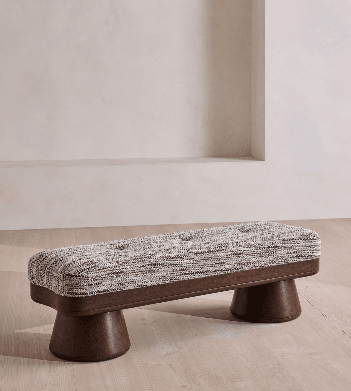 A contemporary rectangular bench featuring a deeply cushioned, tufted upholstered top. The upholstery is a textured, multi-tonal fabric in shades of brown, gray, and white. The base consists of a dark-stained wooden frame from which two substantial, turned wooden pedestal legs descend, providing stable support. The design combines comfort with a modern aesthetic, highlighted by the striking silhouette of the legs. — 3D model