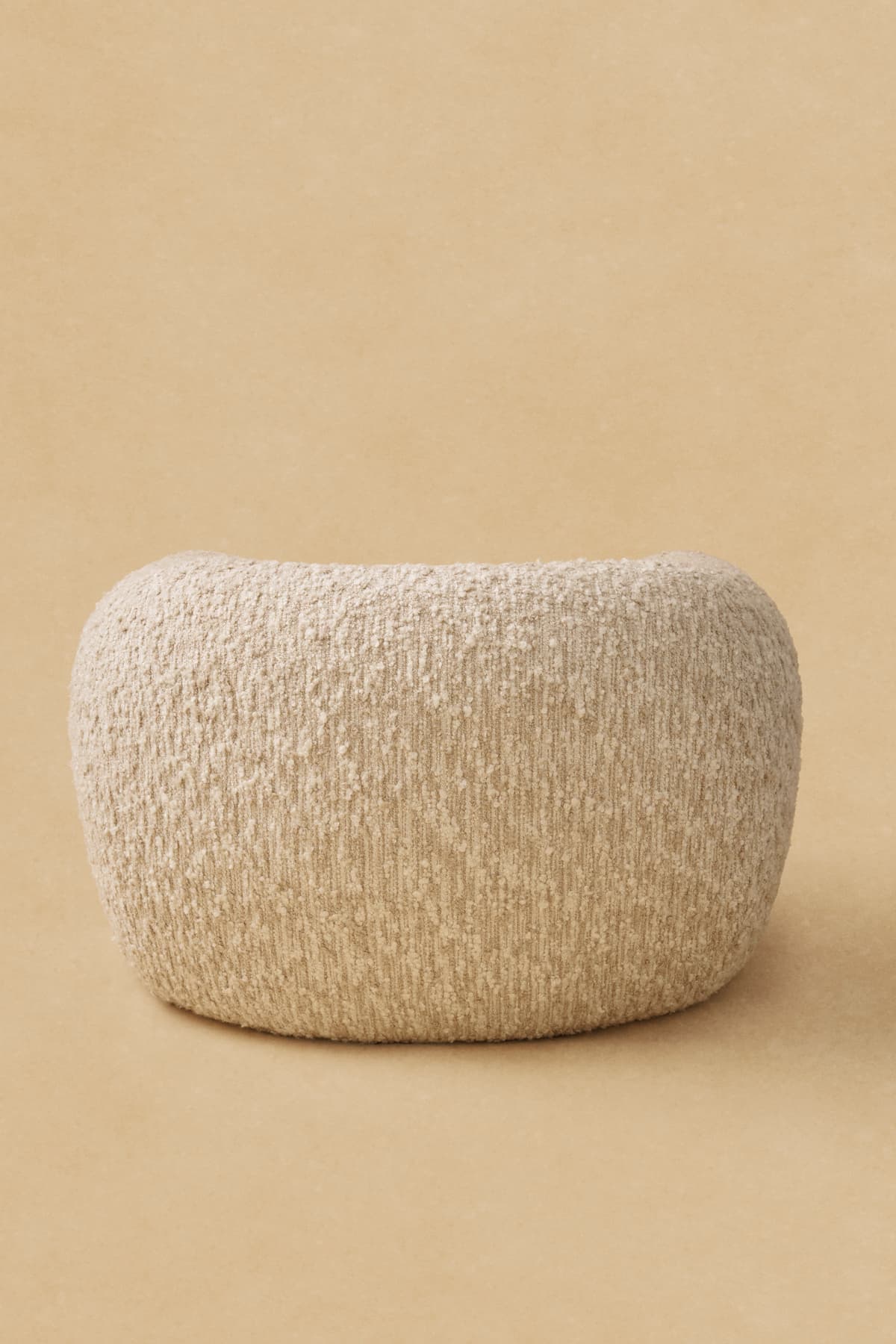 A light beige, rectangular ottoman with rounded edges, upholstered in a textured boucle fabric, appearing soft and minimalist against a plain tan background. — 3D model