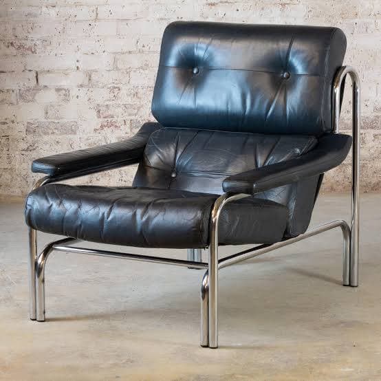 A modernist lounge chair featuring a polished chrome tubular frame and black tufted leather upholstery. The design includes separate, thick cushions for the seat, back, and armrests, all adorned with button tufting. The chair exhibits a low-profile, angular form characteristic of mid-20th-century design. — 3D model
