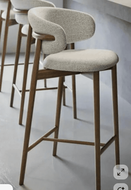 A modern bar stool featuring a light-colored, textured upholstered seat and a curved backrest that integrates seamlessly into a wooden frame. The frame consists of four tapered wooden legs, connected by horizontal stretchers that serve as footrests. — 3D model