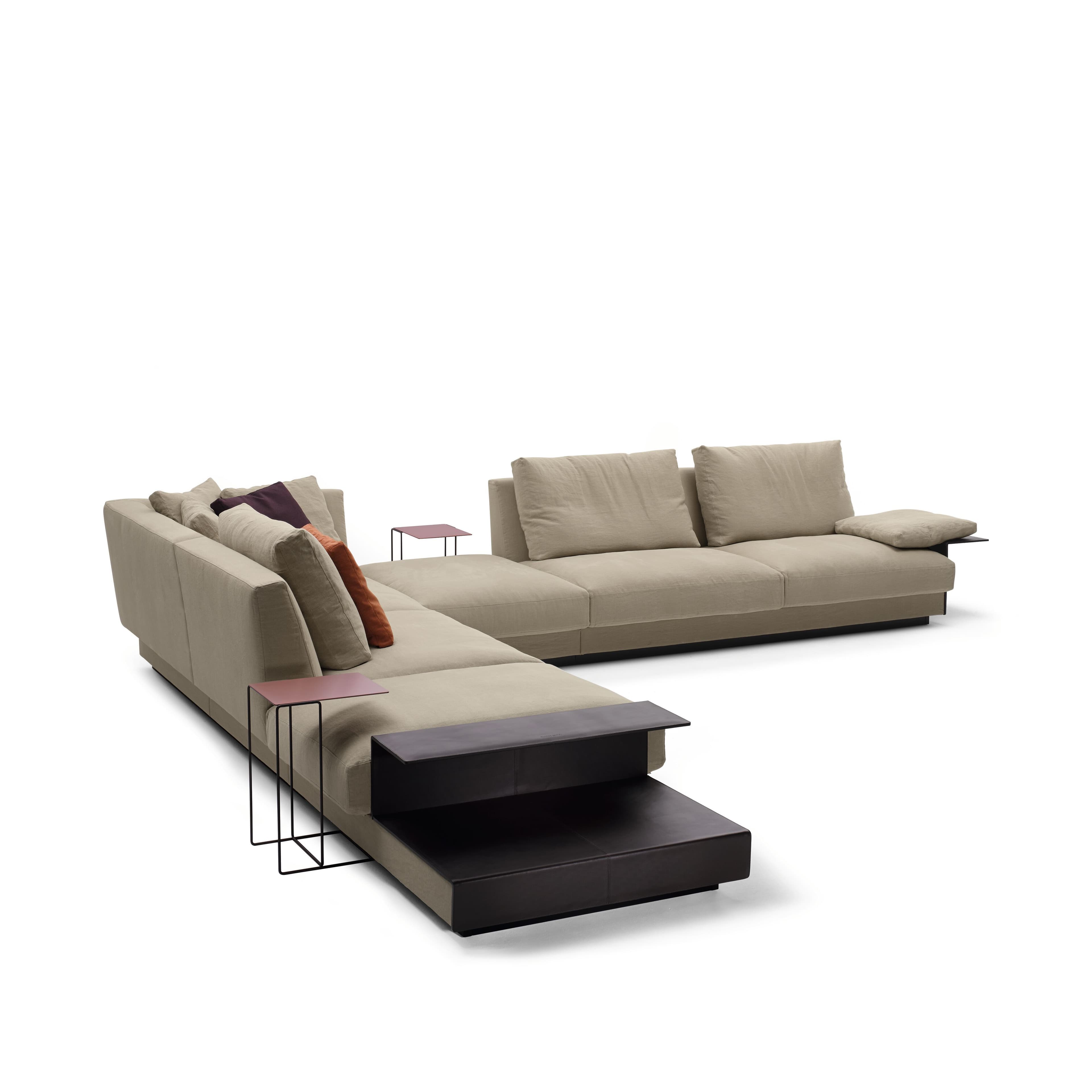 A sectional sofa with a light beige fabric upholstery. The sofa features deep, plush cushions and a modular design, allowing for various configurations. It includes a chaise lounge section and an extended seating area. Accompanying the sofa are two small side tables, one with a dark brown leather surface and a dark metal frame, and another with a reddish-brown metal top and black metal legs. Decorative throw pillows in earthy tones and a darker purple hue are placed on the sofa. — 3D model