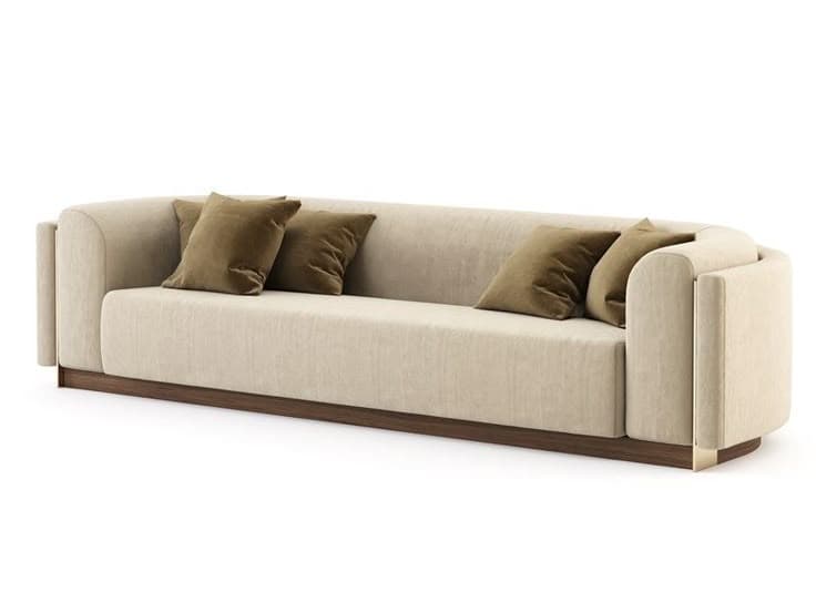A contemporary upholstered sofa featuring a minimalist design with a solid plinth base. The sofa is covered in a light cream or beige fabric, with gently curved and recessed arms. It includes several loose back cushions in a darker olive green or brown velvet fabric. The base is a dark wood, and vertical brass-toned metal accents are visible on the outer sides of the armrests. — 3D model