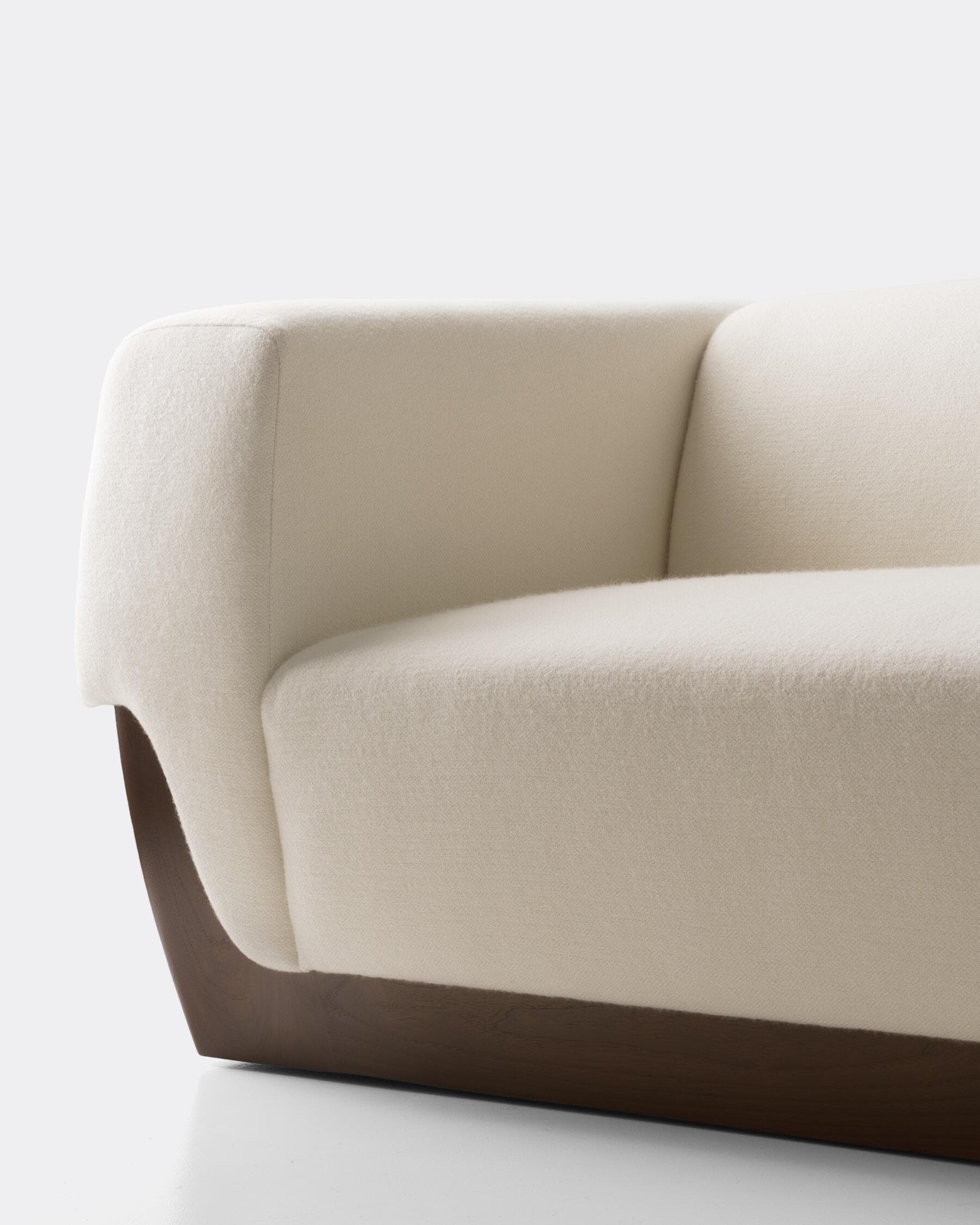 A close-up view of a segment of a modern sofa. The upholstery appears to be a textured fabric in an off-white or cream color. The base of the sofa is constructed from a dark wood, featuring a curved, minimalist design that supports the upholstered section. The contrast between the light fabric and the dark wood base is a prominent design feature. — 3D model