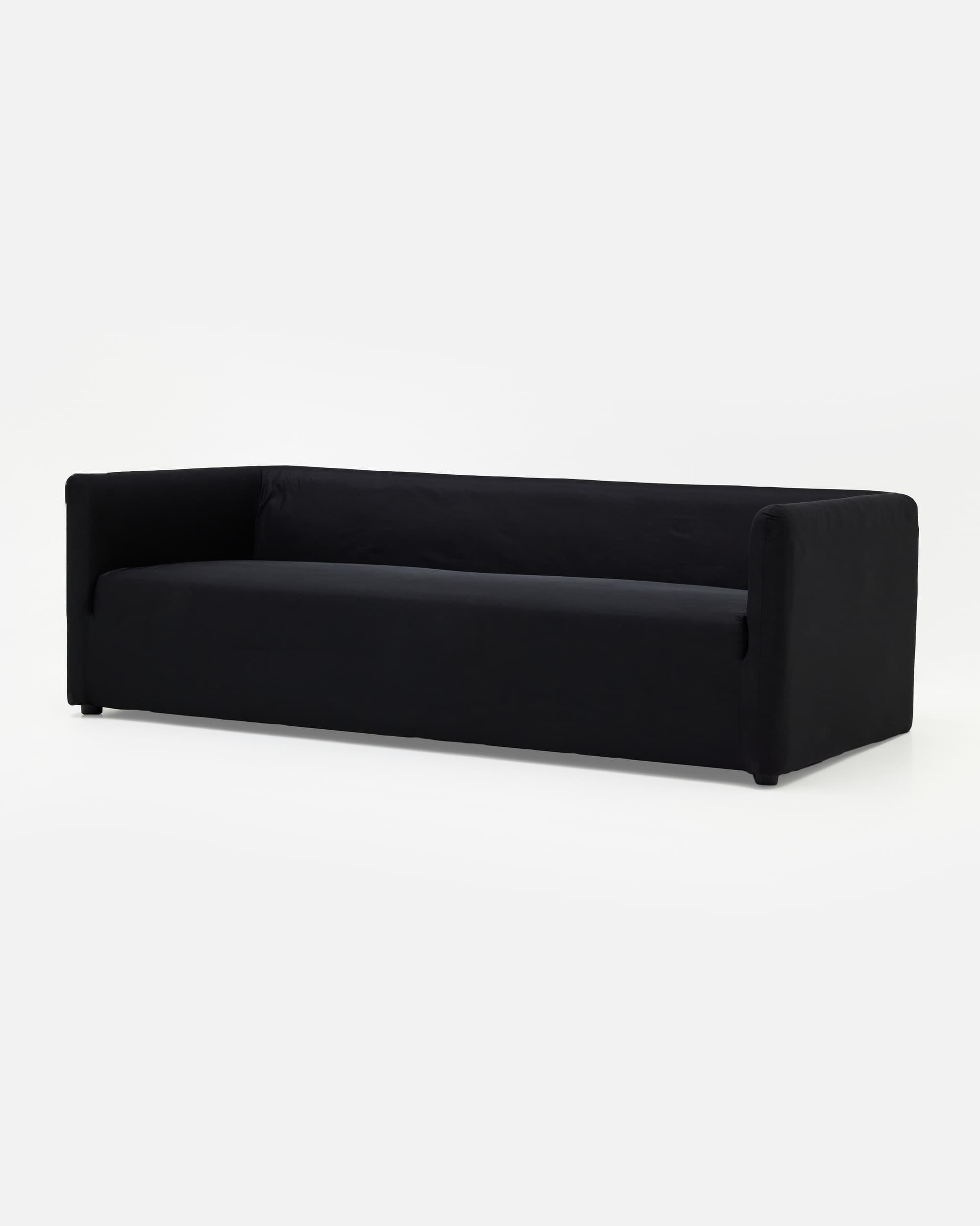 A contemporary three-seater sofa upholstered in plain black fabric, featuring a minimalist design with low track arms and a sleek, low-profile silhouette supported by discreet, recessed block feet. — 3D model