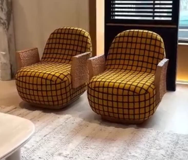 A contemporary lounge chair featuring a distinctive yellow fabric upholstery with a black grid pattern, complemented by unique, rectangular armrests made of a porous, cork-like material. The chair has a rounded, low-profile form. — 3D model