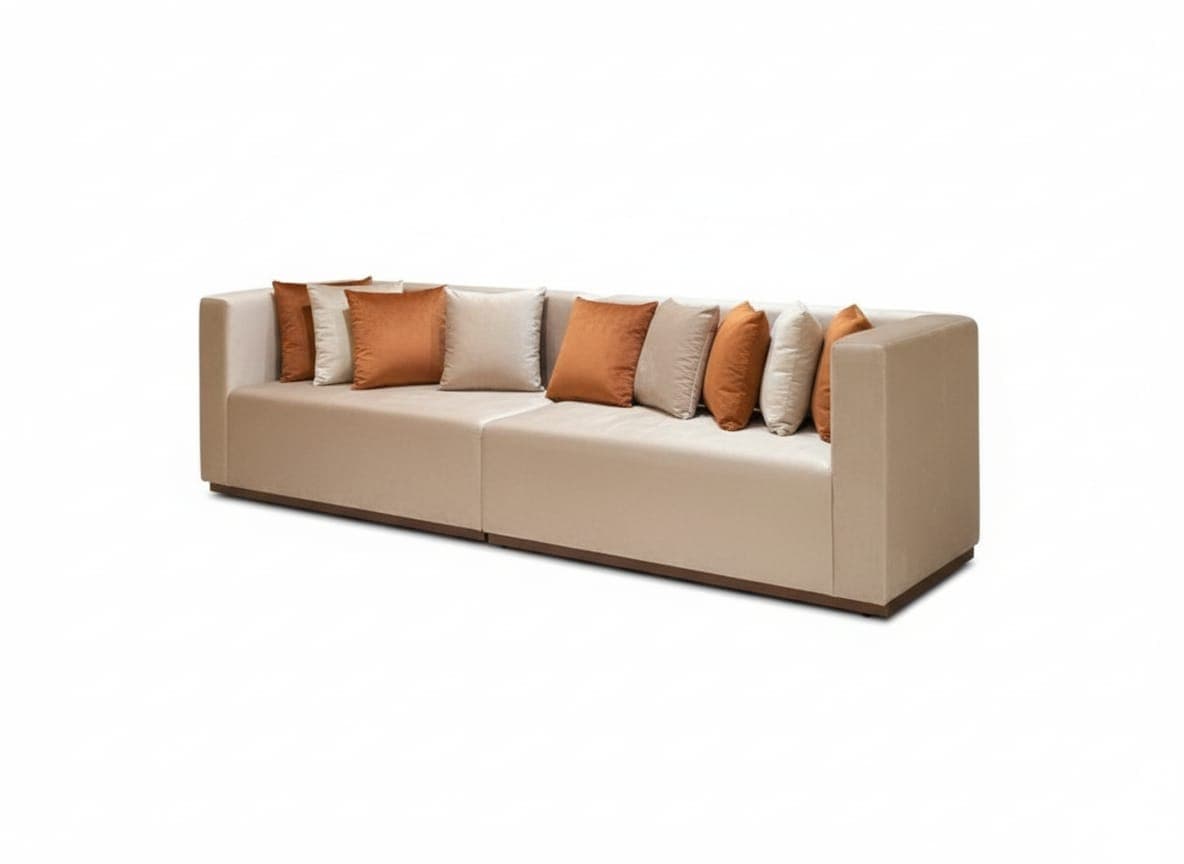 A long, modern sofa with a low profile and clean lines. It appears to be modular, consisting of two sections joined together. The upholstery is a light beige or cream color, and it is complemented by an assortment of decorative throw pillows in shades of burnt orange and beige. The base of the sofa features a dark wooden trim. — 3D model