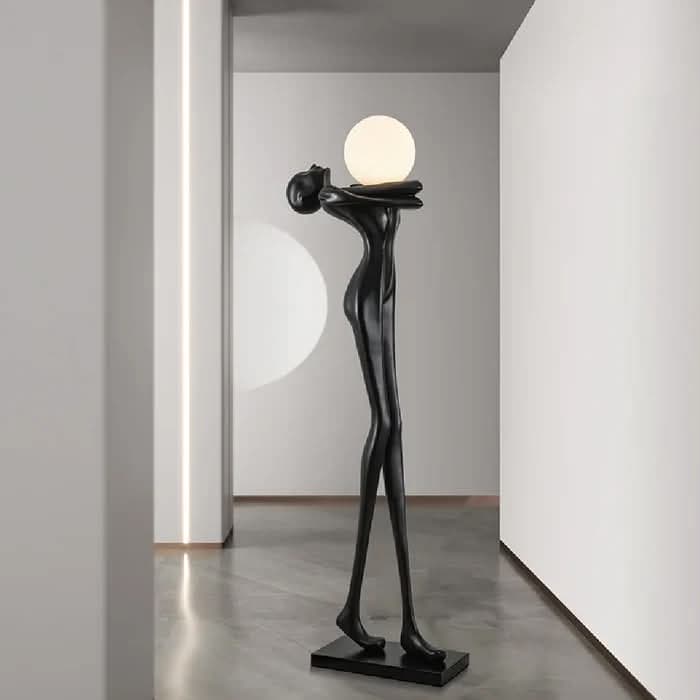 A contemporary floor lamp featuring a sculptural, stylized humanoid figure in black, holding a spherical white light diffuser. The slender figure stands on a flat, rectangular base. — 3D model