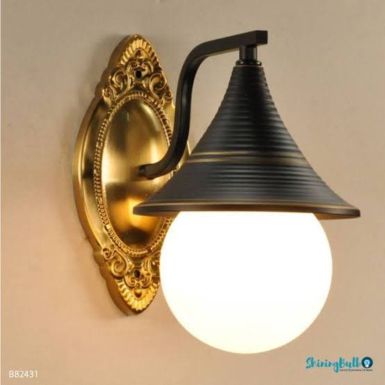 A wall-mounted light fixture featuring an ornate golden oval backplate, a curved matte black arm, a ribbed conical black shade with gold accent bands, and a spherical white glass diffuser. — 3D model