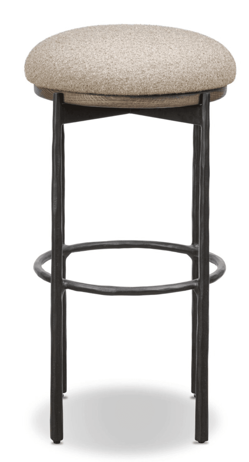 A bar stool featuring a round, upholstered seat made from a light beige, textured fabric, supported by a dark-stained wooden rim. The base consists of four dark, possibly forged or cast metal legs with an uneven, textured surface, connected by a circular metal footrest for stability and comfort. The overall aesthetic combines rustic and industrial elements. — 3D model