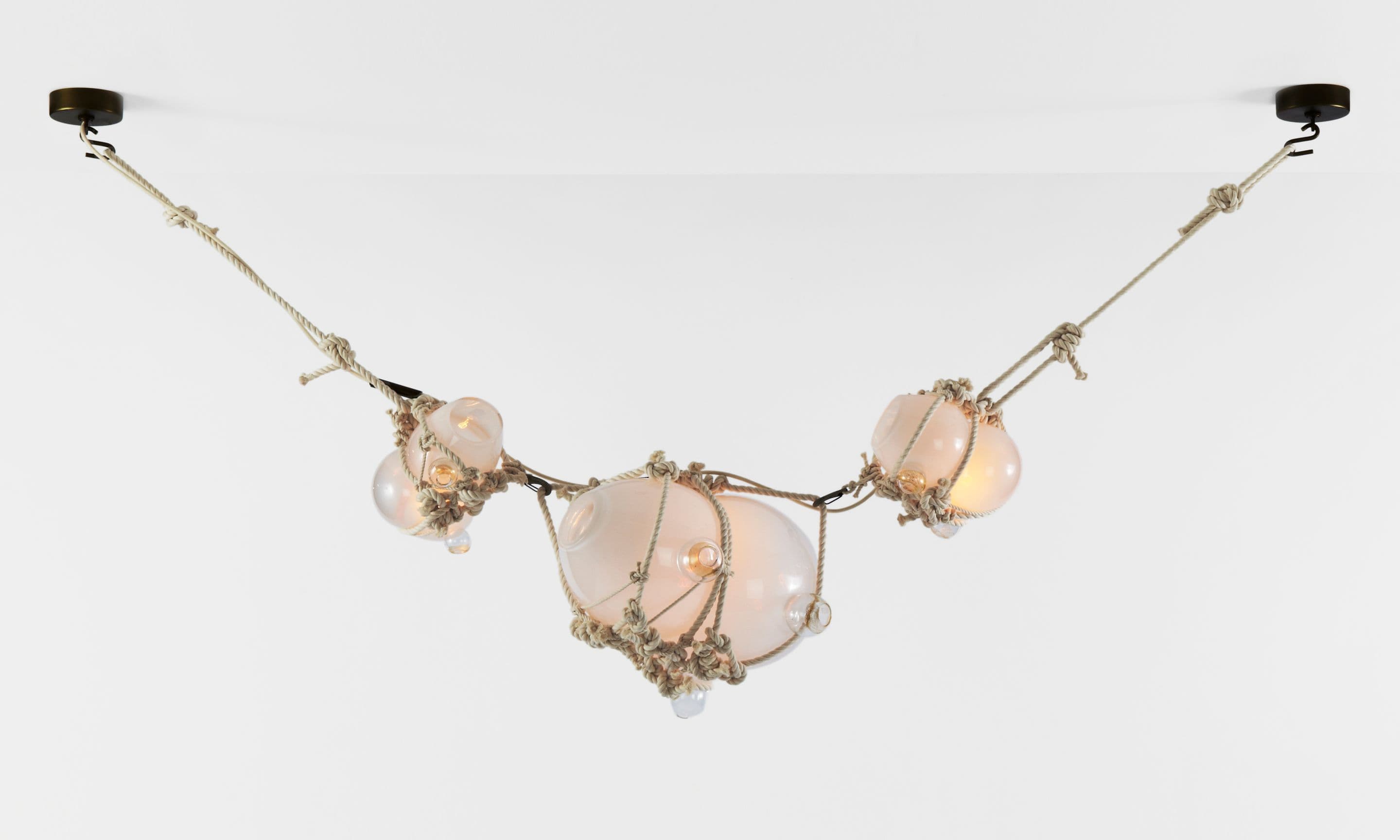 A multi-pendant lighting fixture featuring several glass globes, some clear and some frosted, encased in hand-tied natural fiber rope netting. These individual light elements are suspended horizontally by additional lengths of rope, which are then attached to dark-finished ceiling mounts on either end. The design evokes a nautical or organic aesthetic. — 3D model