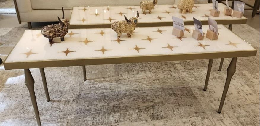 A rectangular console table with a white top featuring a repeating pattern of gold starbursts. The table has a thin gold frame and four slender, tapered legs that curve inwards towards the top and outward towards the bottom, resembling elongated finials. The overall design is sleek and decorative. — 3D model