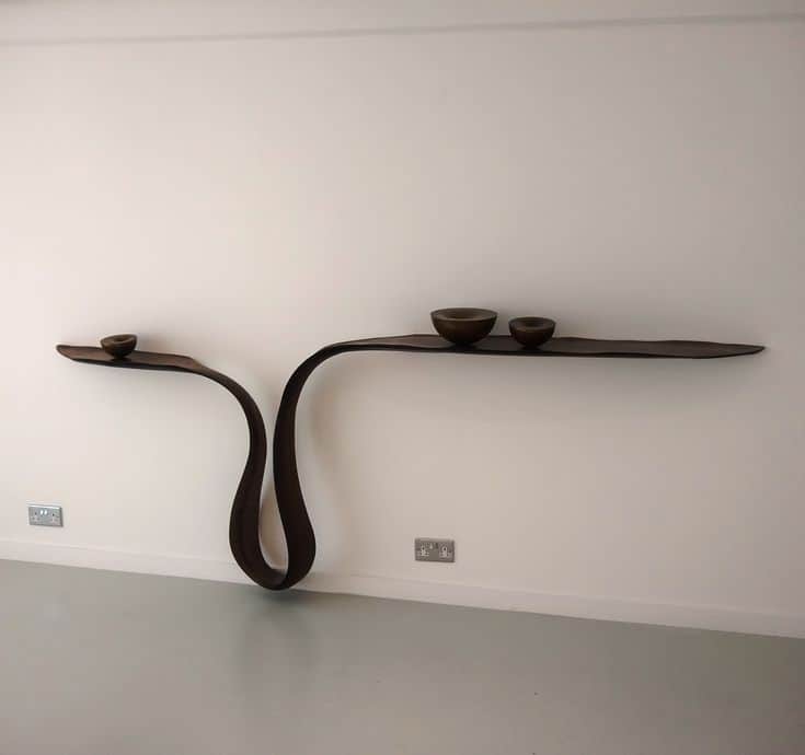 A sculptural, dark wood wall-mounted shelf featuring an organic, undulating ribbon-like form. It int… — 3D model