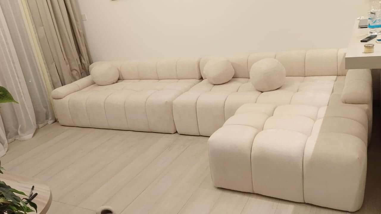 A modular sectional sofa with a tufted, upholstered design. It features a light cream or off-white f… — 3D model