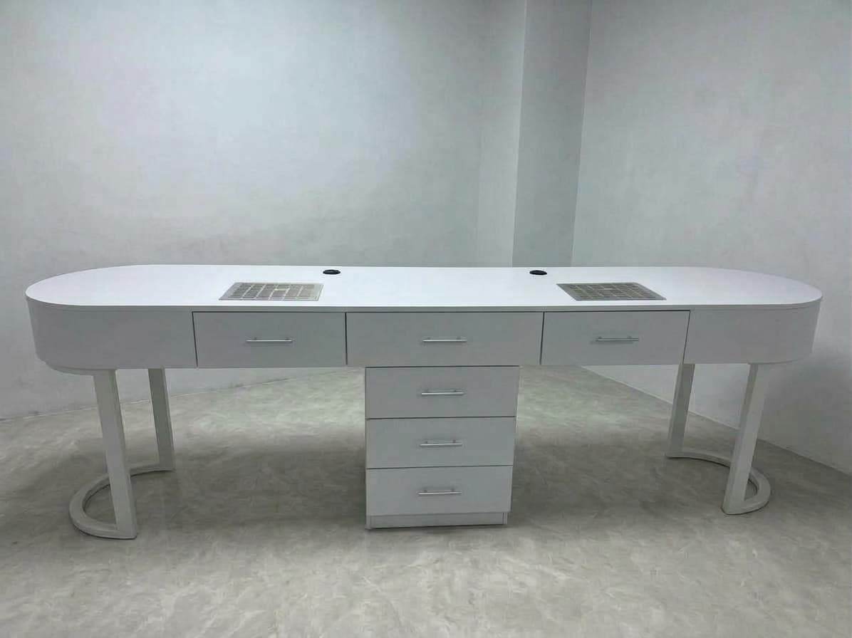 A modern, sleek, white double manicure table featuring an elongated, oval-shaped tabletop. It incorporates two integrated ventilation grates, two circular openings (likely for cords or lights), and ample storage provided by multiple drawers, including a central cabinet unit with four drawers and two smaller drawers on either side of the ventilation grates. The table stands on two stylish U-shaped metal legs and a central cabinet base. — 3D model