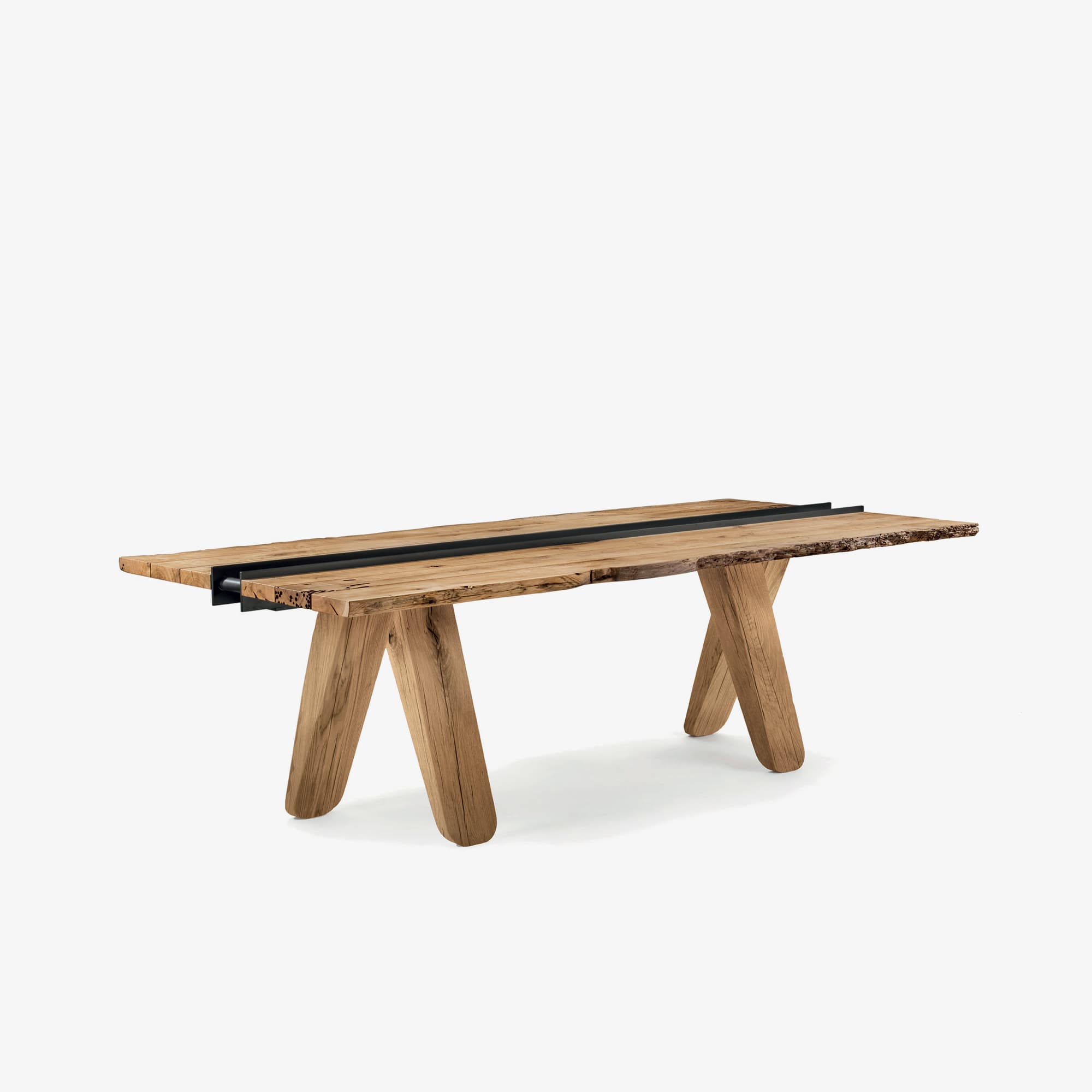 A rustic wooden dining table with a live edge on one side. The tabletop is made of planks with visible grain and natural imperfections. A dark, possibly metal, inlay runs lengthwise down the center of the table, divided into two parallel sections. The legs are angular and made of wood, with a V-shape that tapers towards the bottom. — 3D model