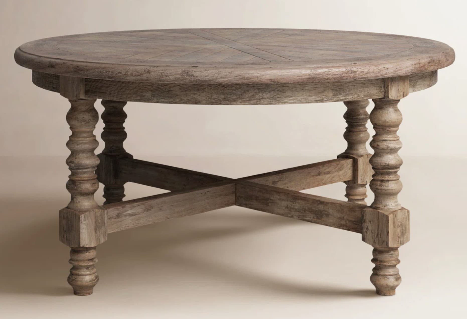A rustic, round dining table with a weathered wood finish. The tabletop features a geometric pattern created by intersecting planks. It stands on four turned legs, each with a bulbous middle section and a square base where they connect to the stretcher. The legs are connected by an X-shaped stretcher assembly. — 3D model