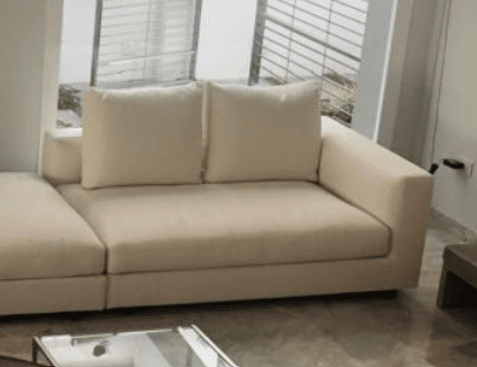 A contemporary modular sectional sofa featuring light-colored fabric upholstery, comprising a main seating unit with a broad armrest and back cushions, and an integrated chaise lounge extension. The design emphasizes clean lines and a minimalist aesthetic. — 3D model
