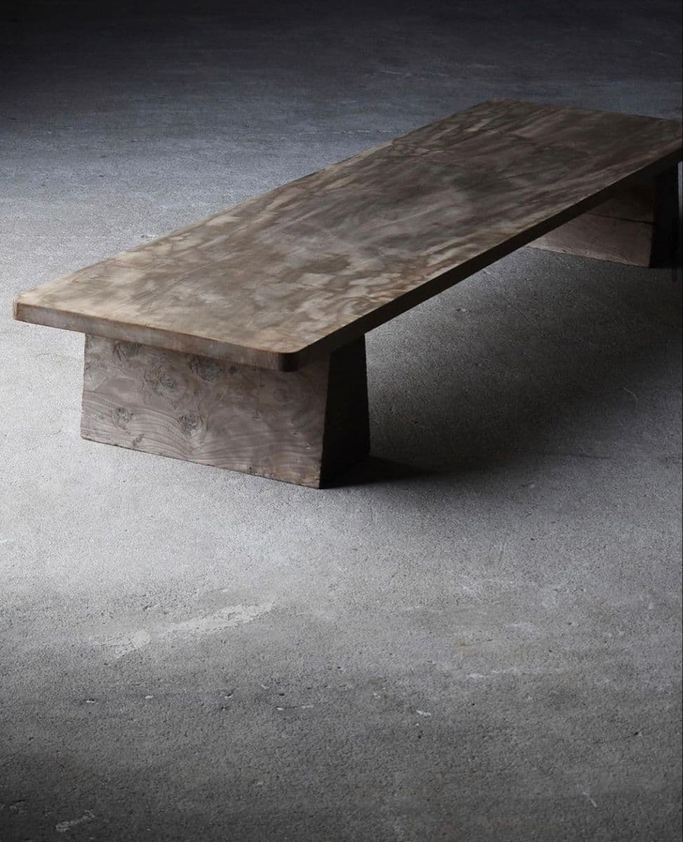 A low, rectangular bench constructed from dark, possibly stained wood, featuring a thick, solid top supported by two robust block-like legs. — 3D model