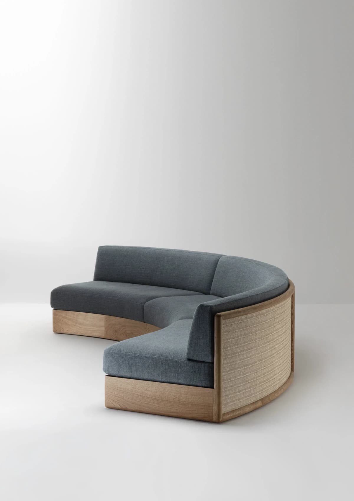 A large, curved sectional sofa featuring gray upholstered seats and backrests, set on a light wood base. The exterior of the curved backrest is paneled with woven cane or rattan. — 3D model