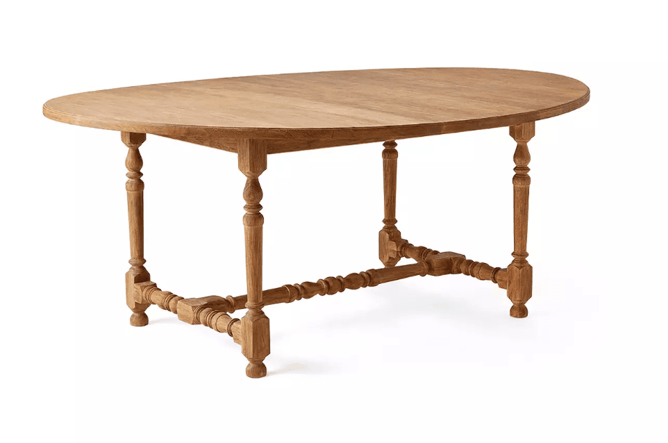 A traditional style oval dining table constructed from light-colored solid wood. It features an oval tabletop with visible wood grain and plank construction. The table is supported by four intricately turned legs, which are connected by a turned stretcher bar at the base, enhancing its classic aesthetic. — 3D model