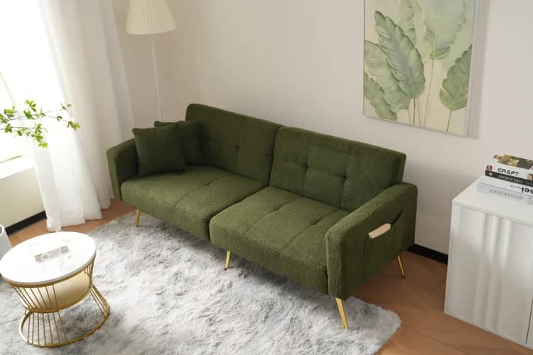 An olive green upholstered sofa bed with a textured boucle fabric, featuring a tufted backrest and golden tapered metal legs. The sofa design suggests convertibility with segmented seat and back cushions. A small green throw pillow and an integrated side pocket are also visible. — 3D model