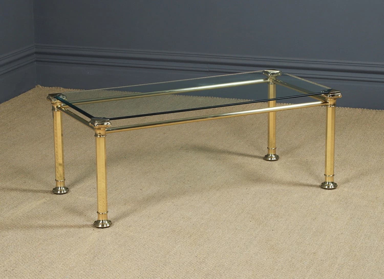 A rectangular coffee table featuring a polished brass tubular frame and a smoked glass top. The design incorporates classical elements such as columnar legs with fluted details and decorative corner finials. — 3D model