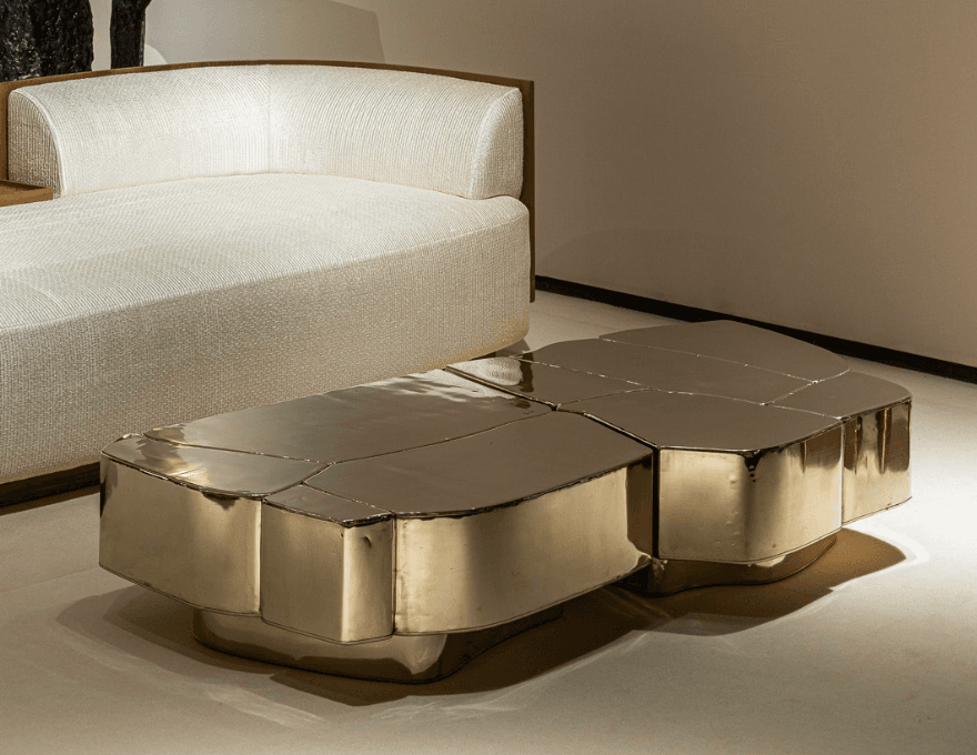A modern, irregularly shaped coffee table constructed from multiple geometric segments that fit together like a puzzle. The surface has a textured, almost faceted appearance, with rounded edges on the side panels and a slightly elevated base. — 3D model