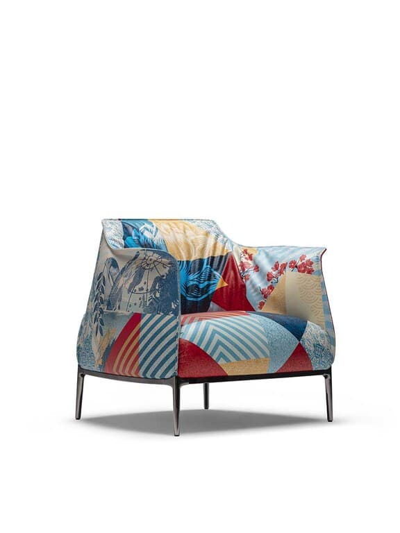 A modern armchair upholstered in a patchwork fabric featuring various graphic patterns and imagery, including what appears to be Asian-inspired motifs. The armchair has a relatively low profile with flared armrests and a gently curved backrest. It is supported by four slender, dark-colored metal legs that angle outwards. — 3D model