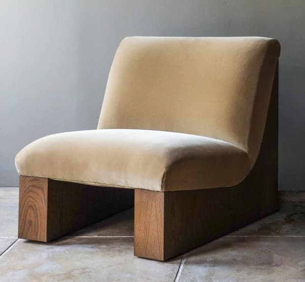 A contemporary armless lounge chair featuring a plush, upholstered seat and backrest in a light beige/tan velvet, supported by a distinct, dark-stained solid wood block base. — 3D model