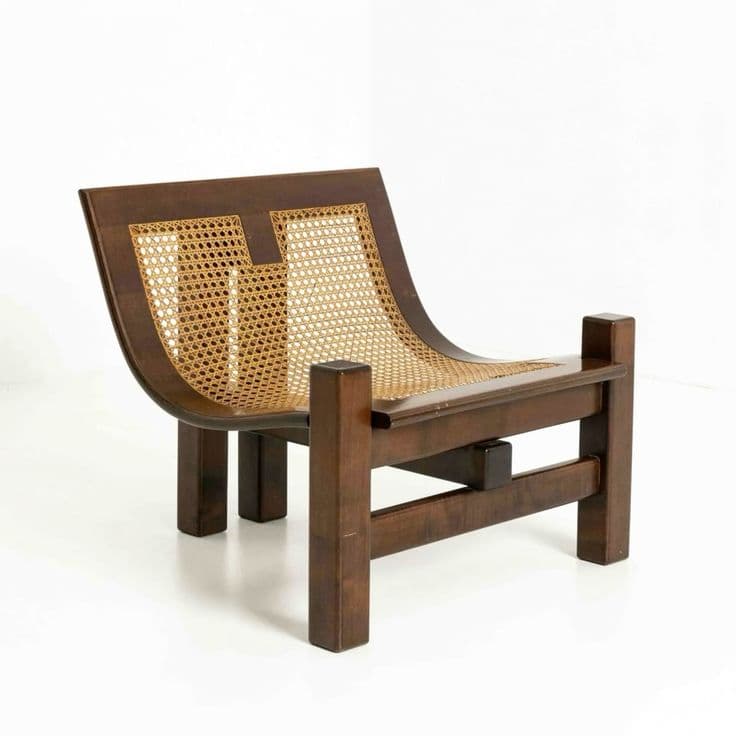 A low-profile lounge chair featuring a sturdy dark stained wooden frame with a curved backrest and seat, both intricately woven with natural cane. The chair exhibits a robust, almost brutalist aesthetic due to its thick, rectangular wooden elements for legs and frame, contrasting with the lighter, organic texture of the cane. — 3D model