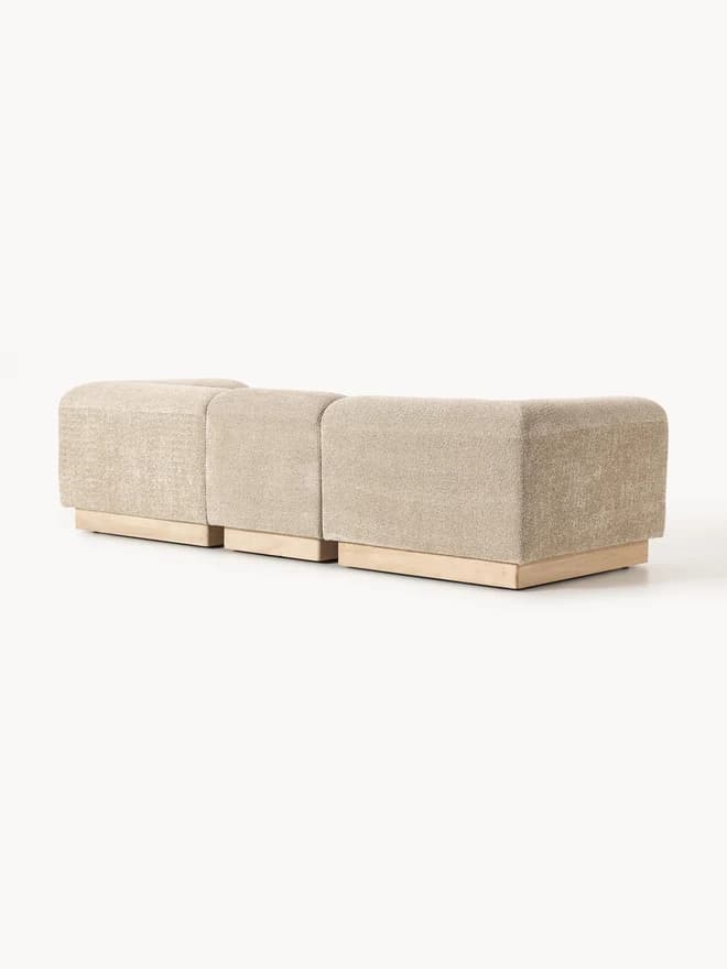 A modular upholstered bench consisting of three individual, backless sections. Each section is covered in a textured, light beige fabric and sits upon a recessed base made of light-toned wood. The design is contemporary and minimalist, emphasizing clean lines and a low profile. — 3D model