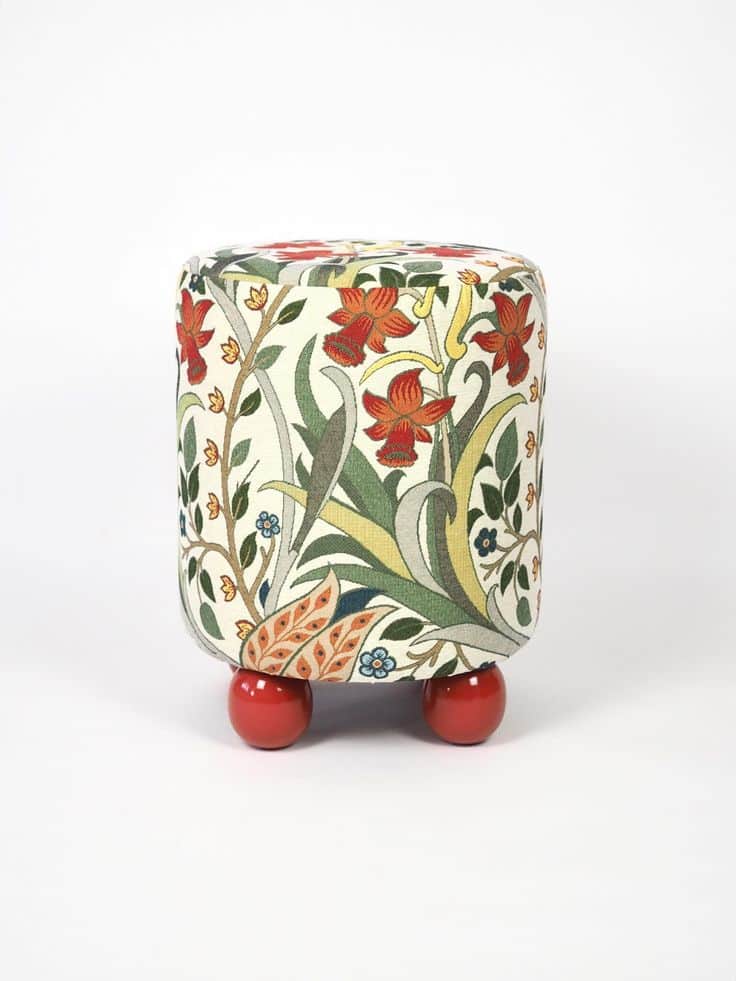 A compact, cylindrical ottoman upholstered in a multi-colored fabric featuring an intricate Arts and… — 3D model