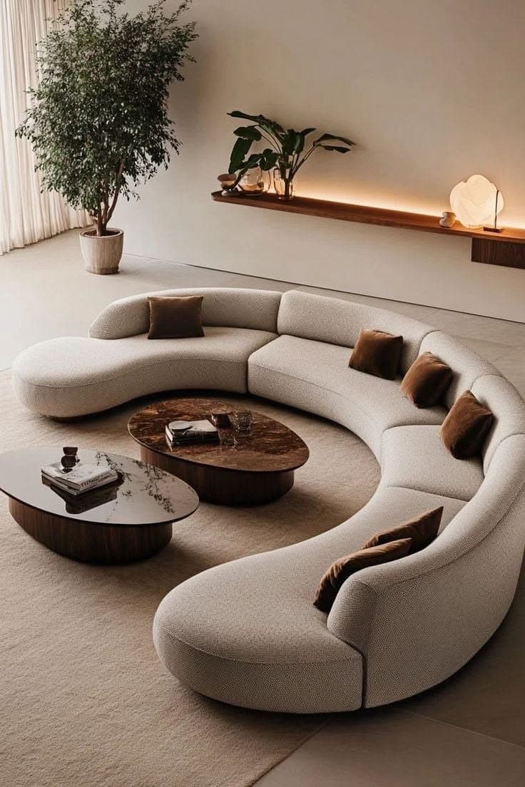 A large, modular, curved sofa with a low profile. The sofa features rounded edges and is upholstered in a textured white fabric. It is composed of several connected sections, forming a crescent shape. Several throw pillows in a contrasting brown color are placed on the seating surface. — 3D model