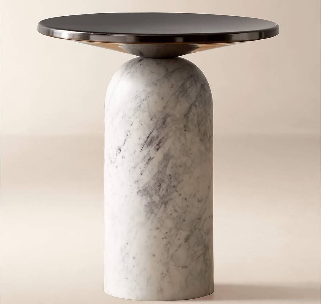 A modern accent table featuring a solid, cylindrical white marble base with grey veining, topped by a circular, dark-colored metal surface. The marble base has a smooth, rounded arch at its upper end, providing a soft transition to the table top, which appears to be a dark bronze or blackened metal, slightly concave on the underside. The overall design is minimalist and sculptural. — 3D model