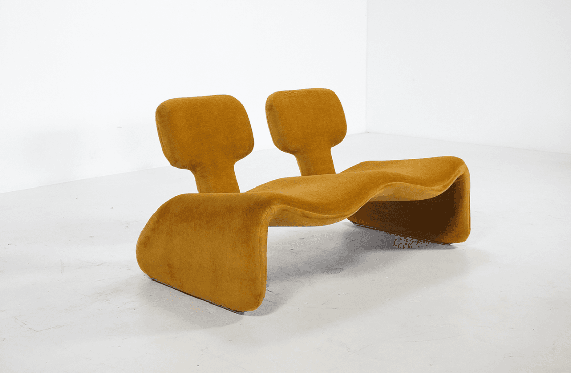 An organic modern double chaise lounge, characterized by its undulating S-curve form and fully upholstered in a mustard yellow fabric. It features two integrated, paddle-shaped headrests, suggesting a design for two users to recline comfortably in a relaxed position. — 3D model