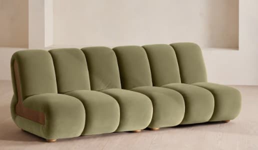 A contemporary sofa featuring a plush, olive-green upholstered finish composed of multiple rounded, channel-tufted segments forming the seat, backrest, and armrests. The sofa has a low profile with a distinctive curved, natural wood panel integrated into one end, serving as both a design accent and part of the armrest structure. The overall aesthetic is soft, organic, and modern. — 3D model