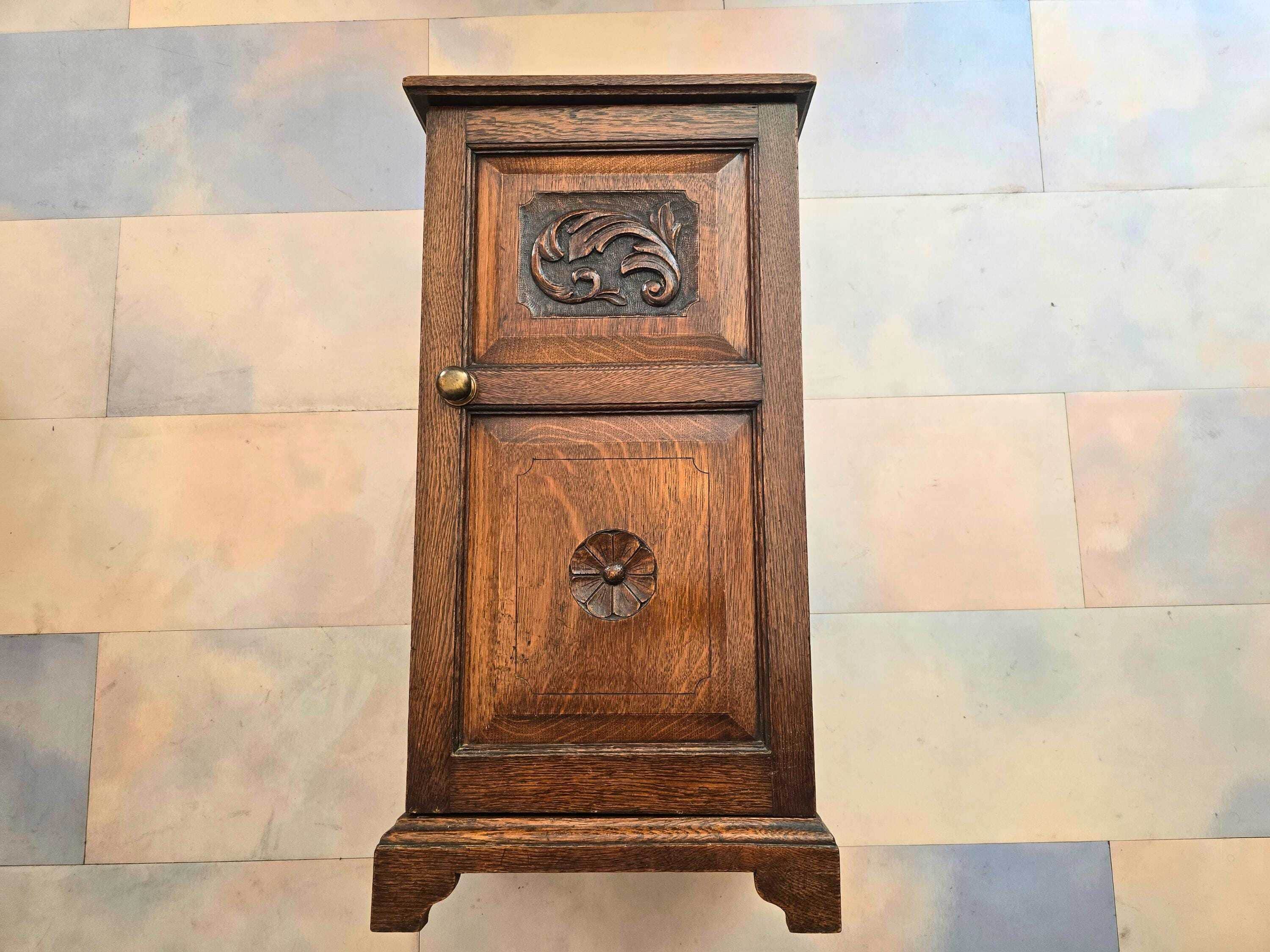 A small, dark brown wooden cabinet featuring a single door adorned with two distinct ornate carvings… — 3D model