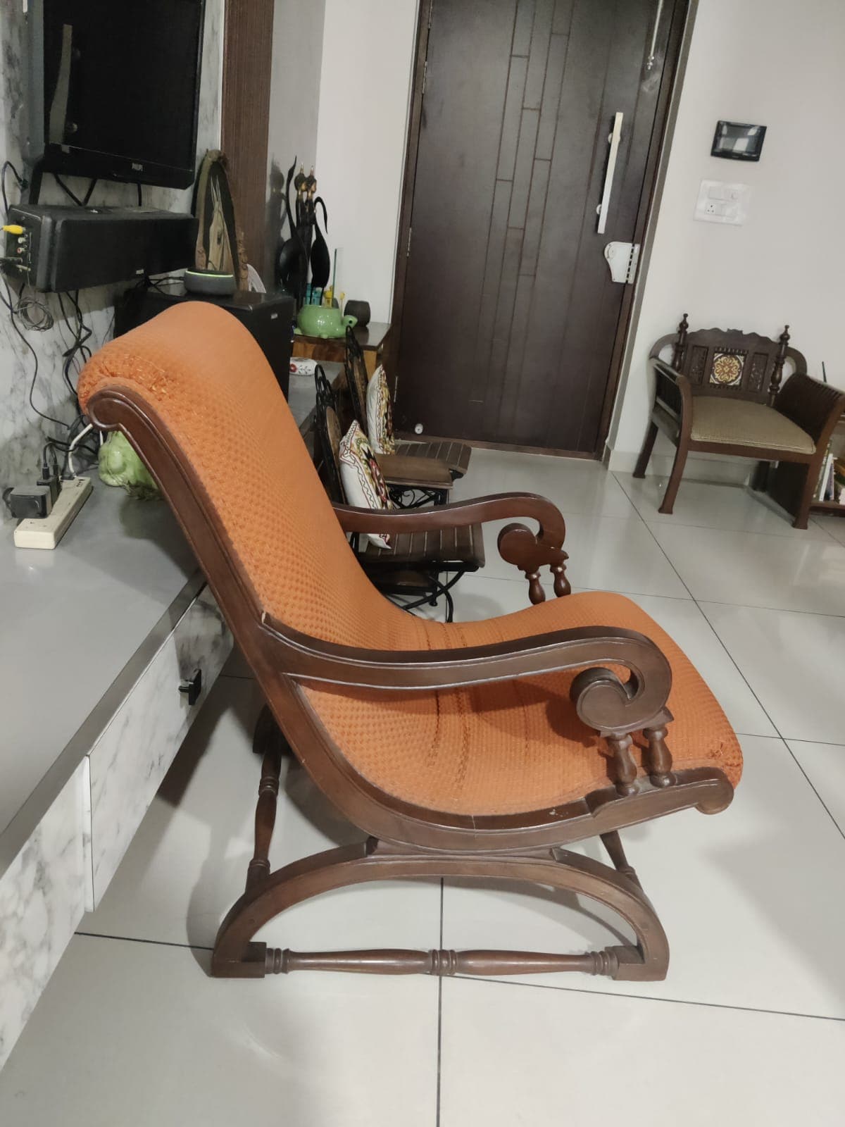 A traditional rocking chair featuring a dark-stained wooden frame with carved details and ornate armrests, paired with textured orange-brown upholstered seat and back cushions. The chair is designed with classic curved rockers allowing for a gentle back-and-forth motion. — 3D model
