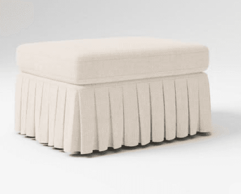 A rectangular upholstered ottoman featuring a padded top cushion and a pleated fabric skirt that conceals its base. The item is rendered in a light, neutral beige fabric with a subtle texture, presented against a clean white background. — 3D model