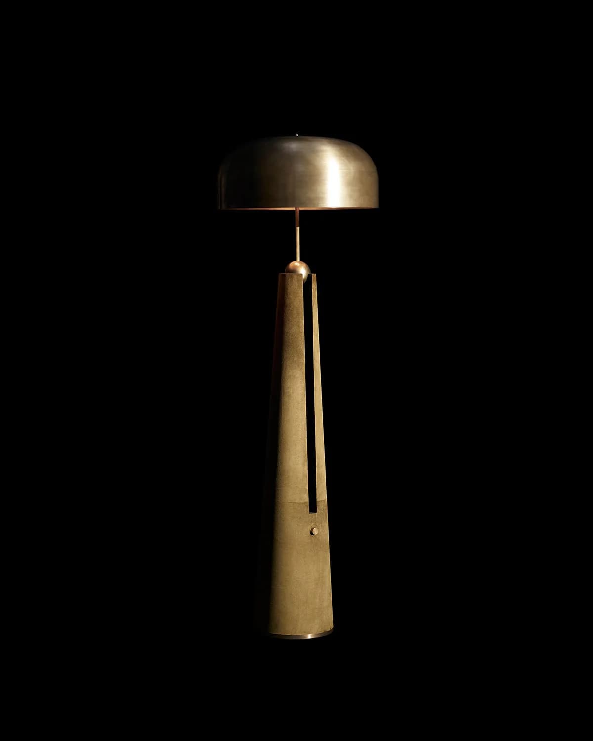 A tall, modern floor lamp constructed from brass, featuring a tapered, geometric base with a vertical channel and a spherical detail, supporting a slender stem that culminates in a wide, hemispherical shade. The light source is housed within the domed shade, directing illumination downwards. — 3D model